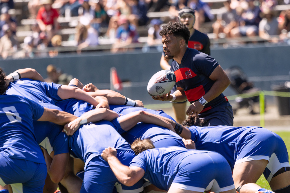 Men's rugby player Inoke Waqavesi holds the ball next to a scrum of BYU players, April 2024