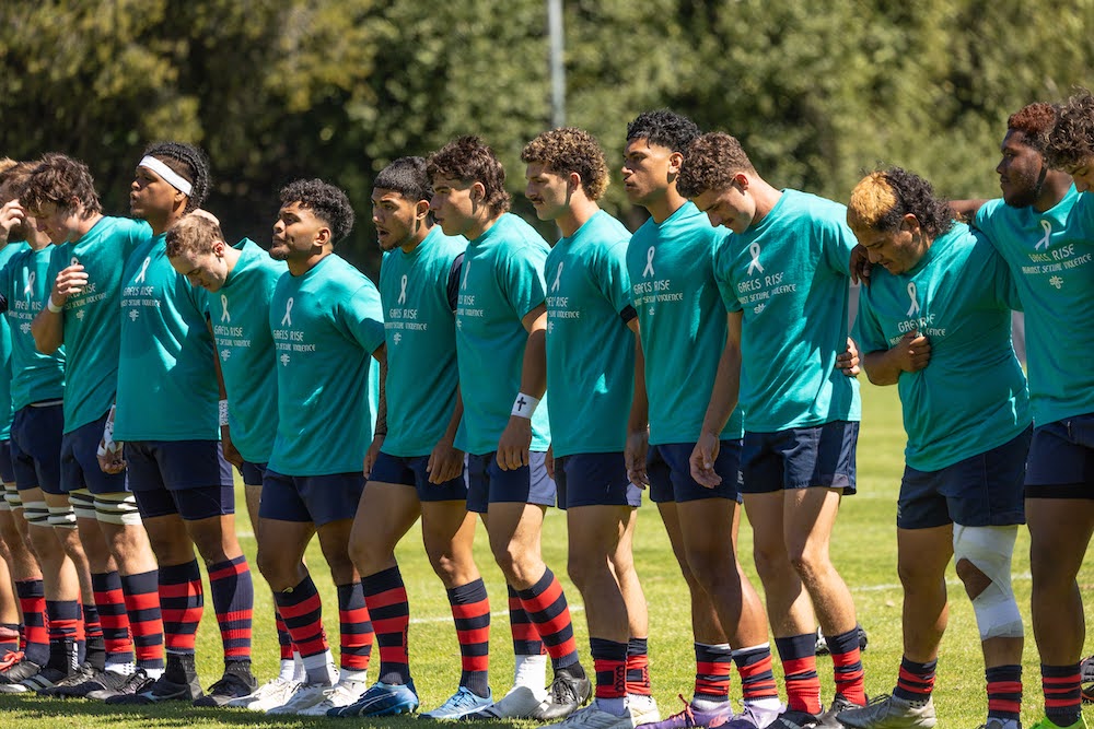 Men's rugby players stand in a row wearing teal T-shirts emblazoned with Gaels Rise Against Sexual Violence