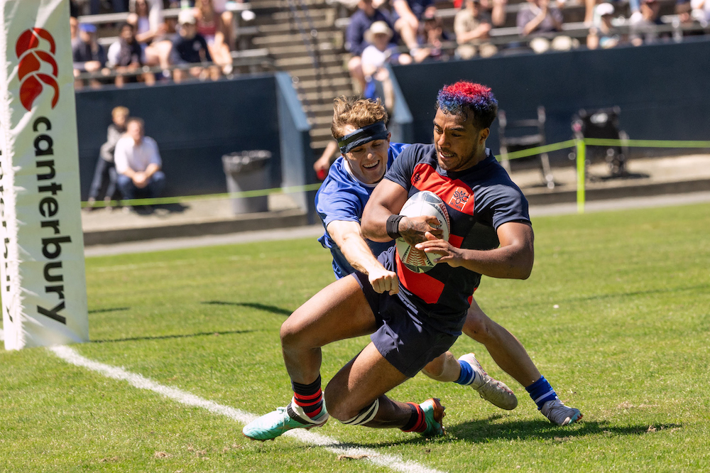 Men's rugby player Kaipono Kayoshi carries the ball across the try line, while a BYU defender tries to stop him, April 2024