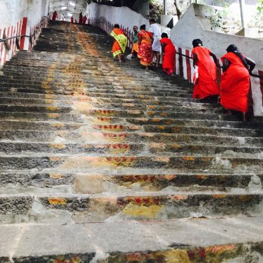 People in bright orange walk up a long staircase of old stone steps to a temple.