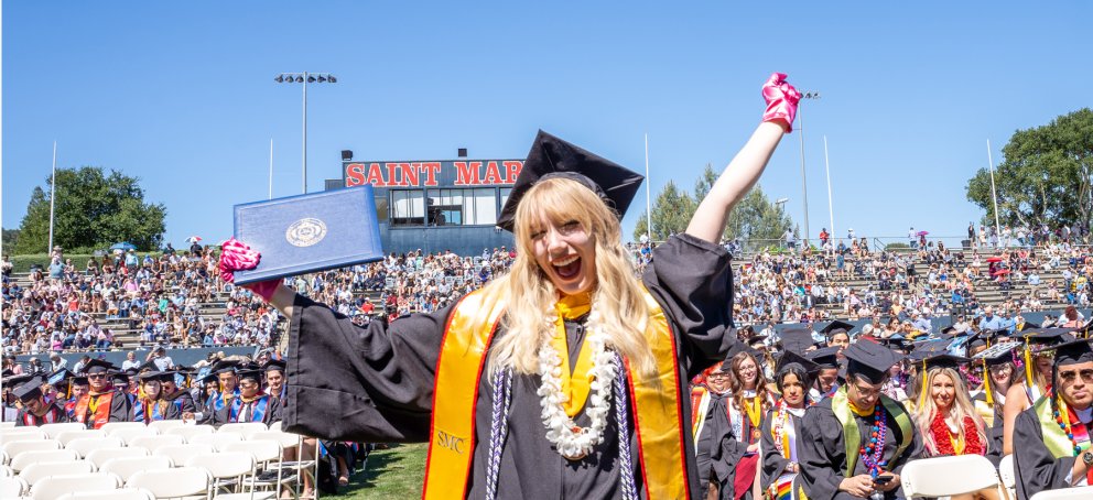 A student at commencement holding up her diploma wearing the womens and gender studies pink gloves