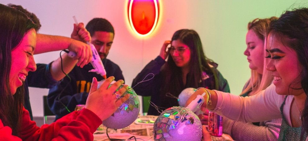 six students sitting around a table making disco balls out of mirrors and hot glue