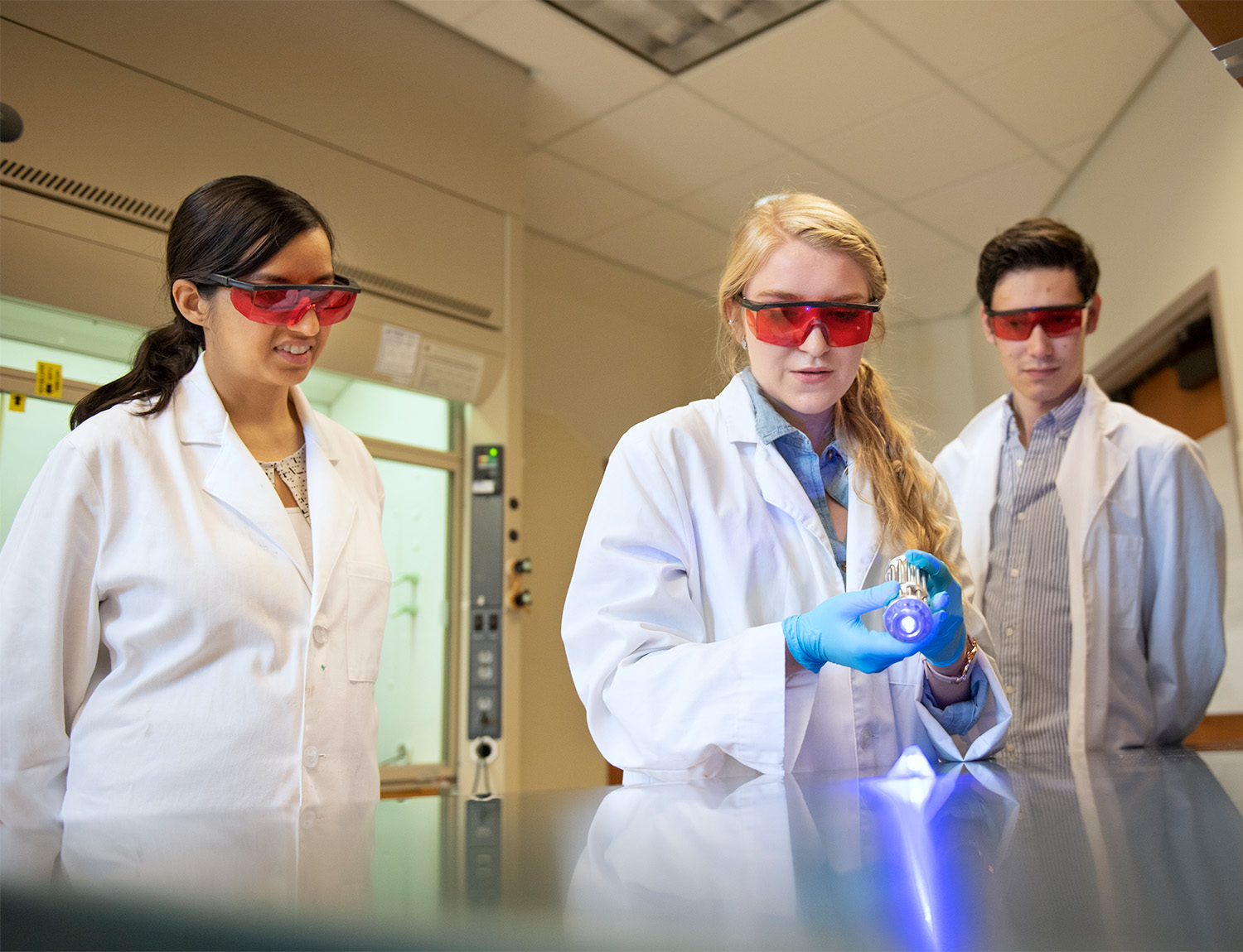 students in lab coats and protective glasses work on an experiment