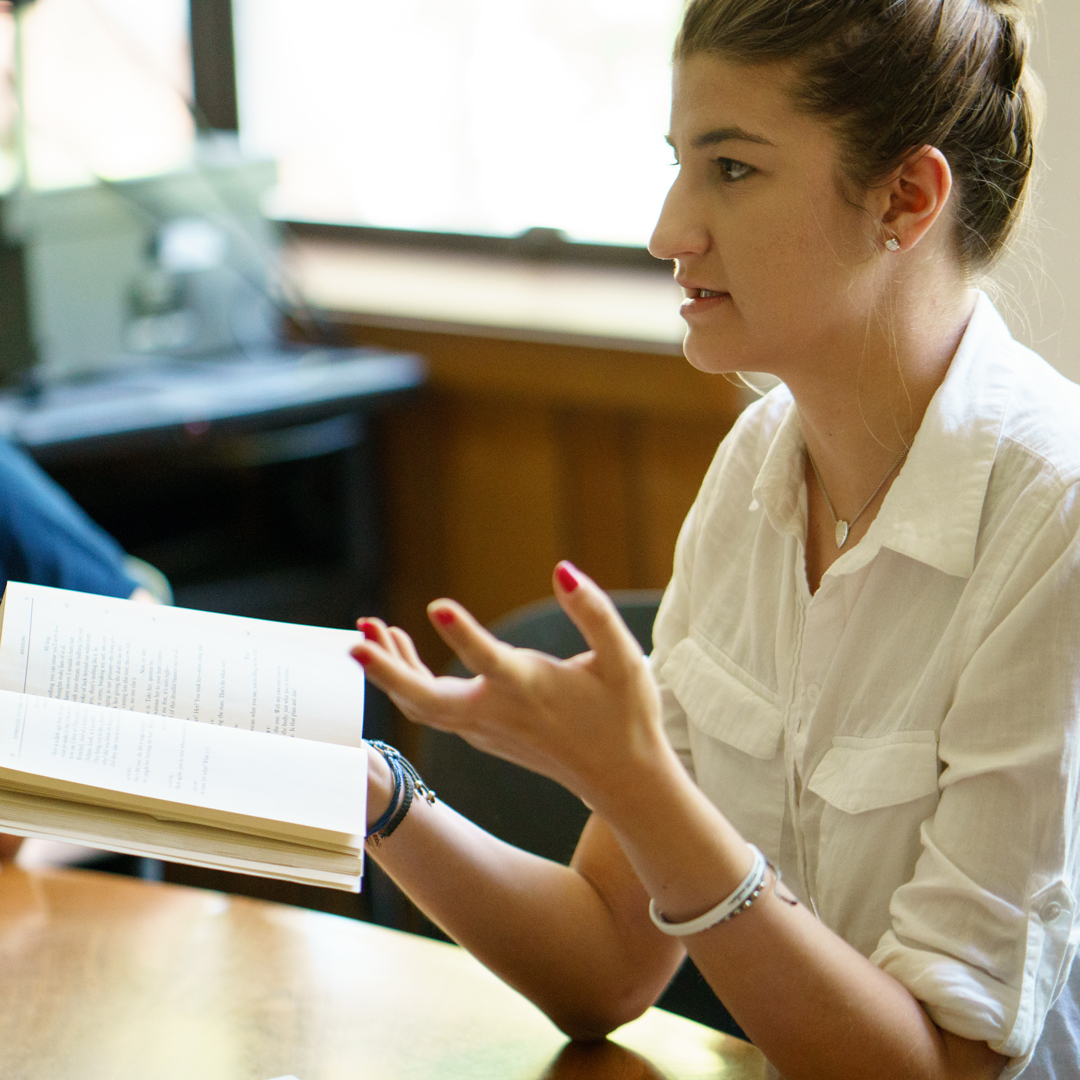 A student gesturing while holding a book in class
