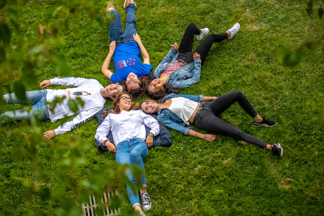 Students laying on the grass with their heads together in a star shape