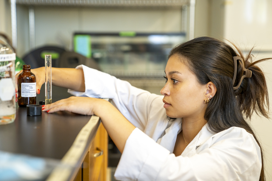 A student in a lab is eye level with the table, looking at a sample she just poured