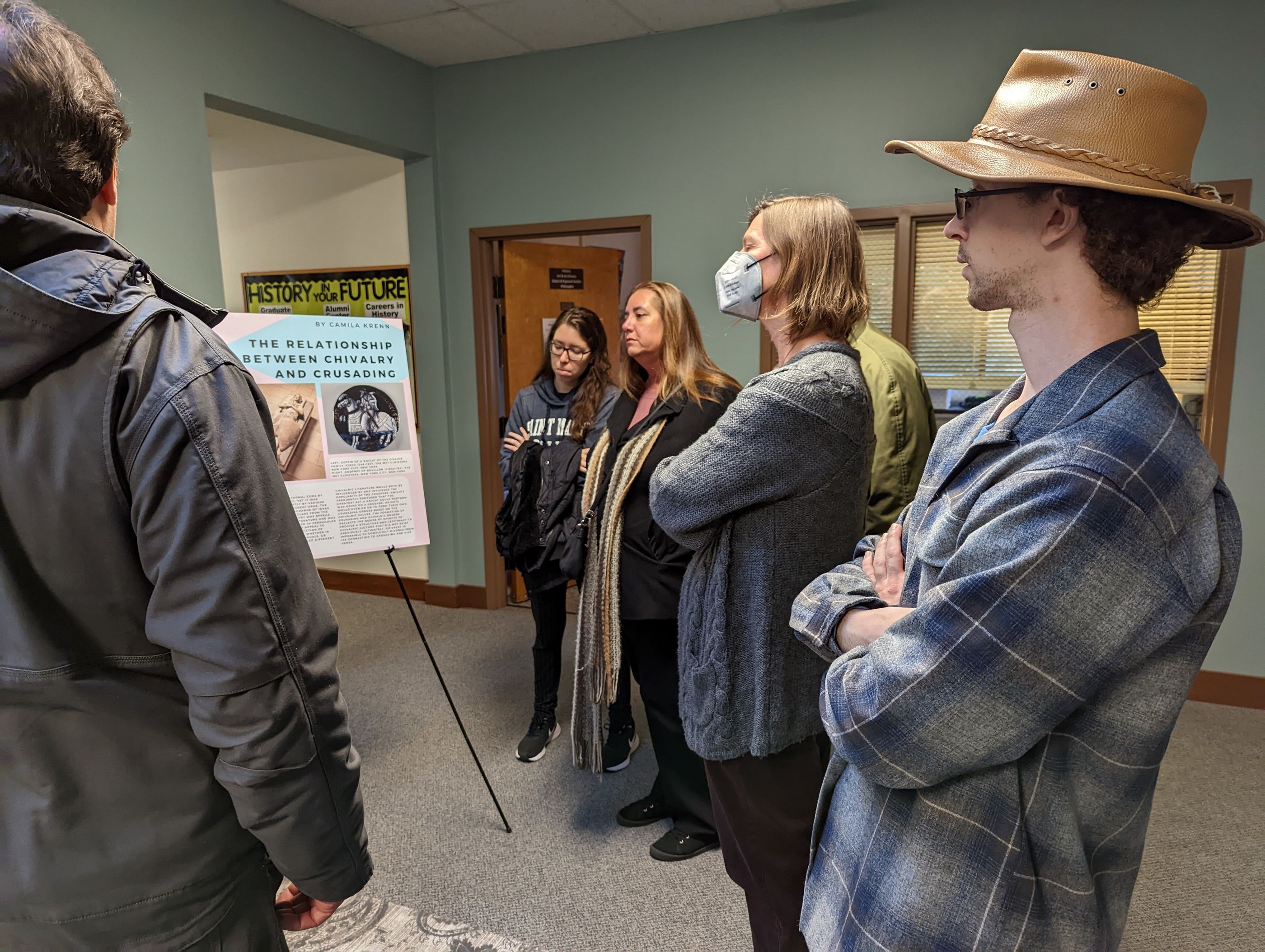 people standing and listening to a student talk about their thesis