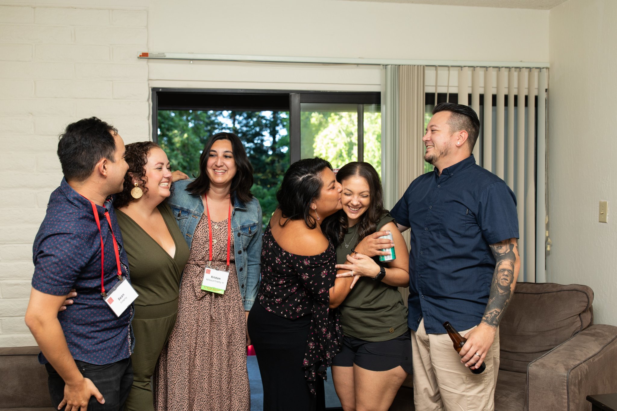 Six people embrace and laugh inside a townhouse living room
