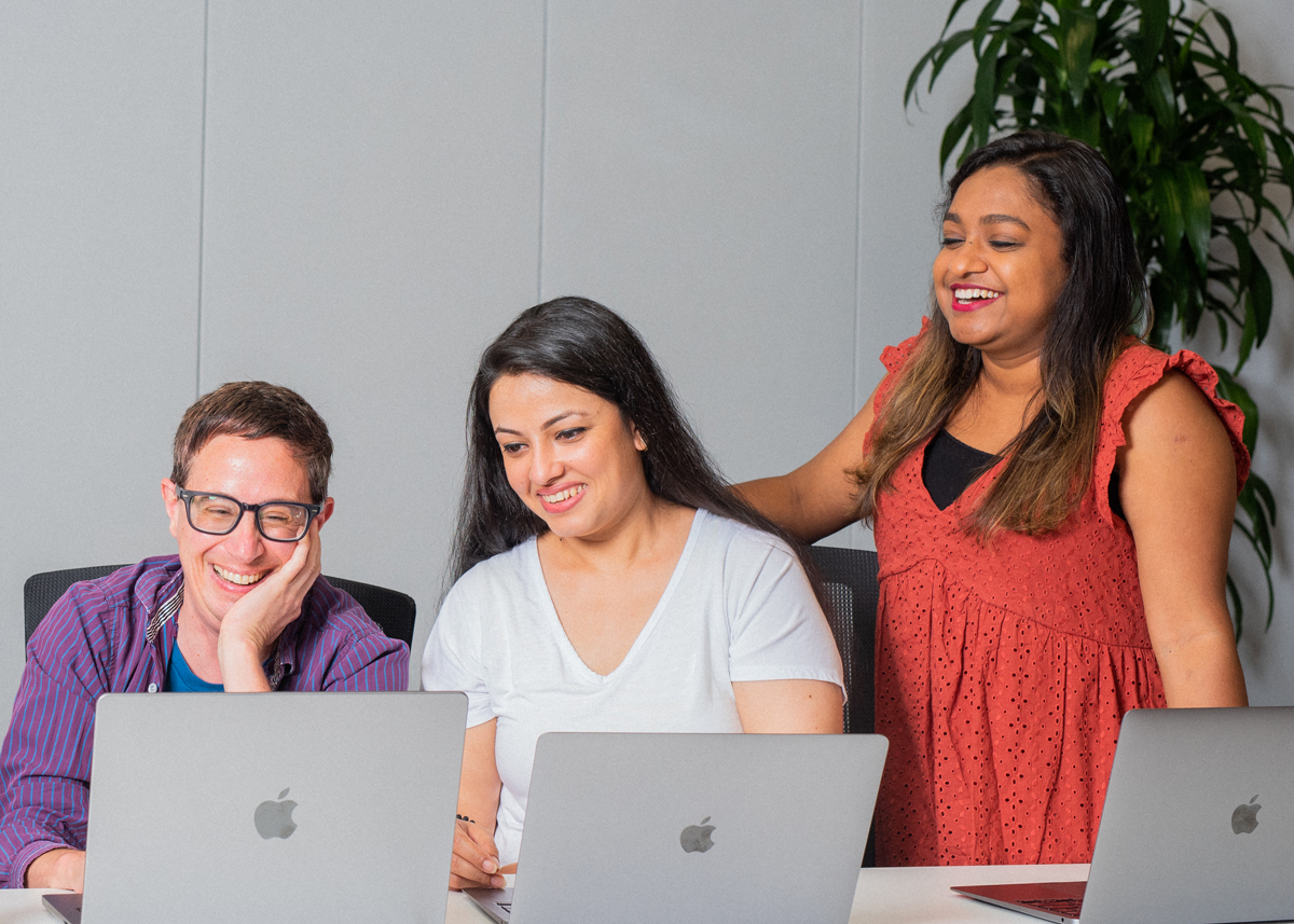 Three people with laptops are smiling and talking