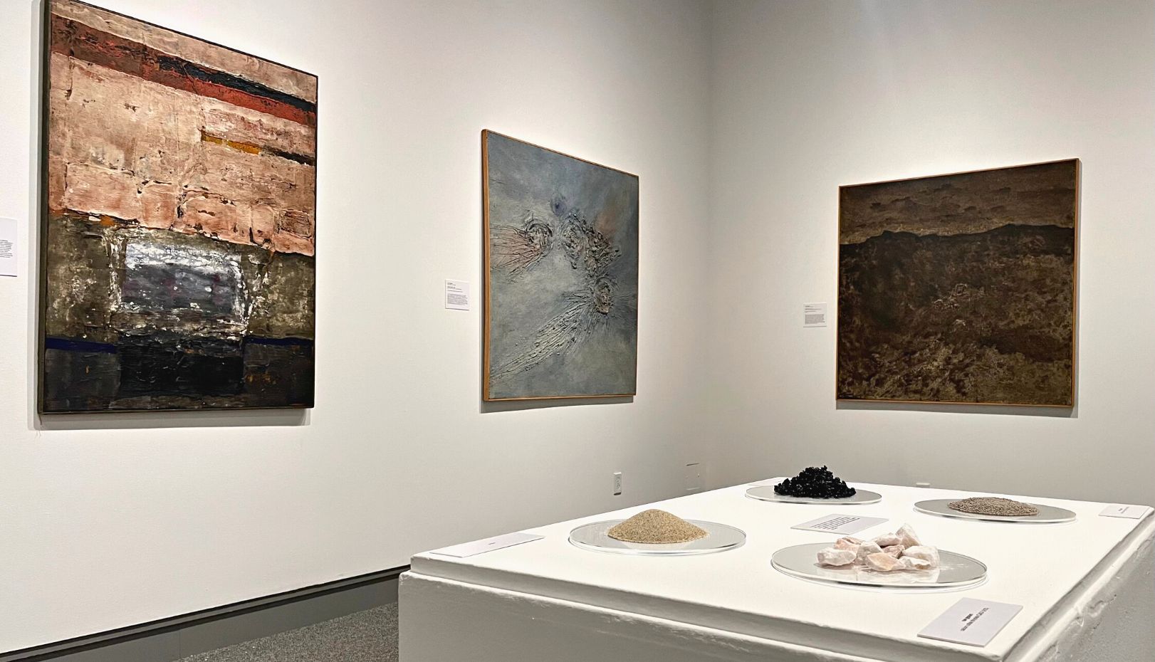Installation image of From the Ground Up showing paintings and earth materials of asphalt, gypsum and sand.