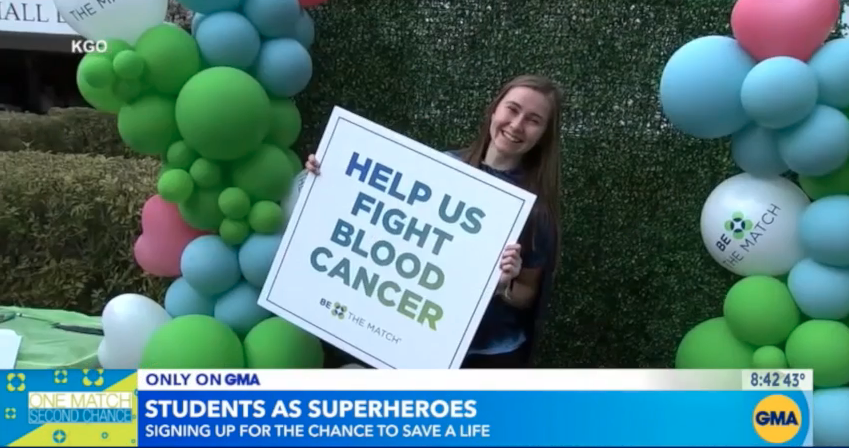 A female Saint Mary's student holds a sign that says "Help Us Fight Blood Cancer"