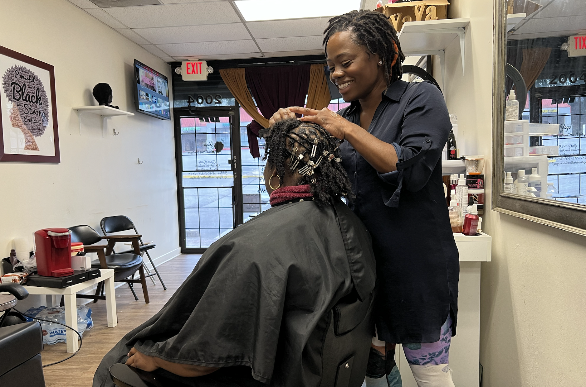 A woman sits in a salon chair while a hair stylist works on her hair.