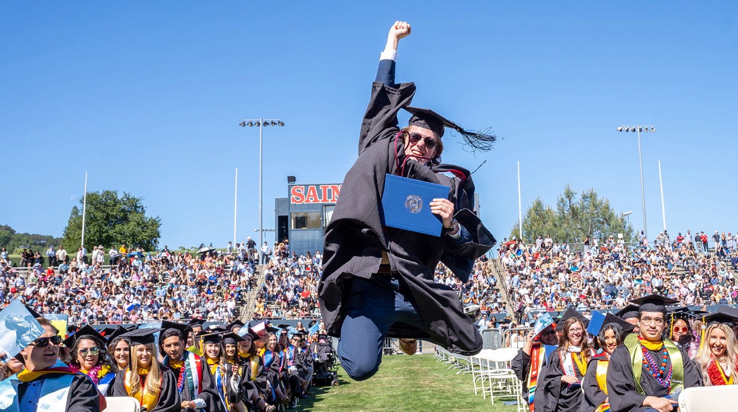 student jumping for joy on sunny graduation day