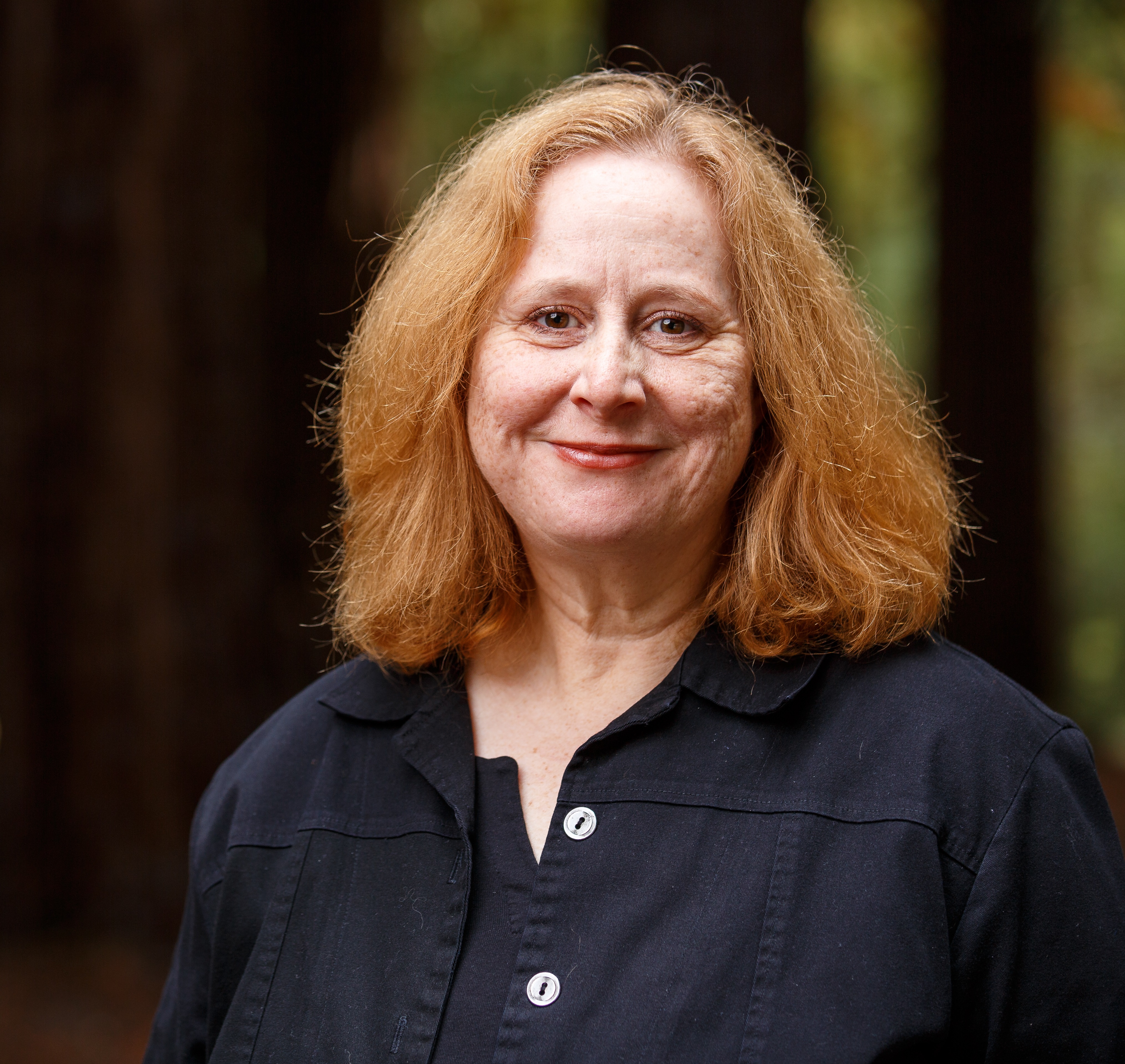 headshot photo of Prof. Marilyn Abildskov with redwood trees in background