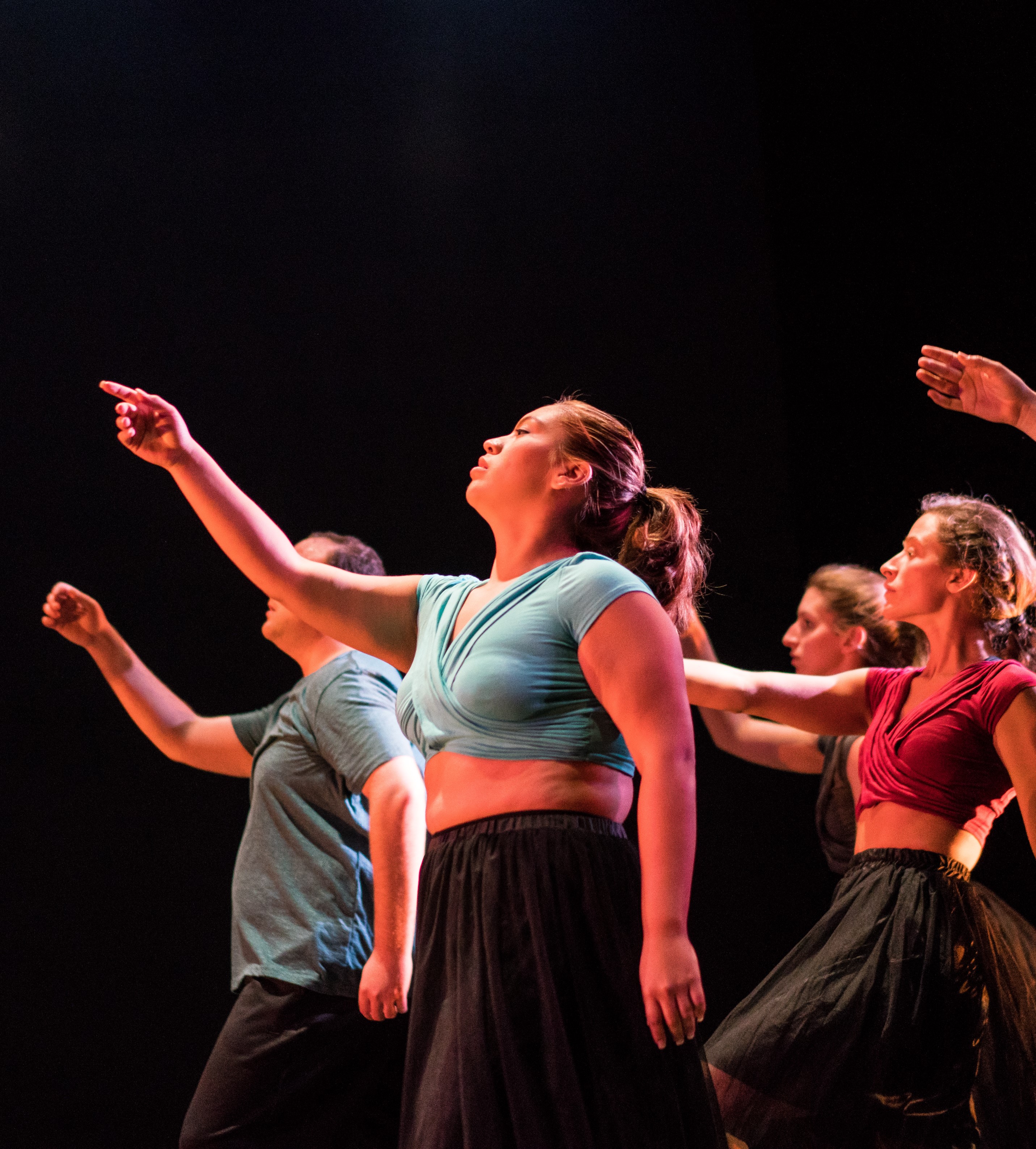Five graduate Dance students pointing upwards in front of a black curtain.
