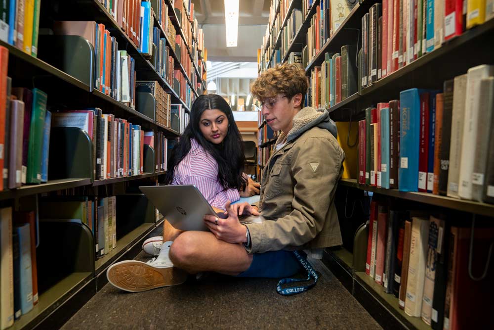 two students sitting in the library book stacks