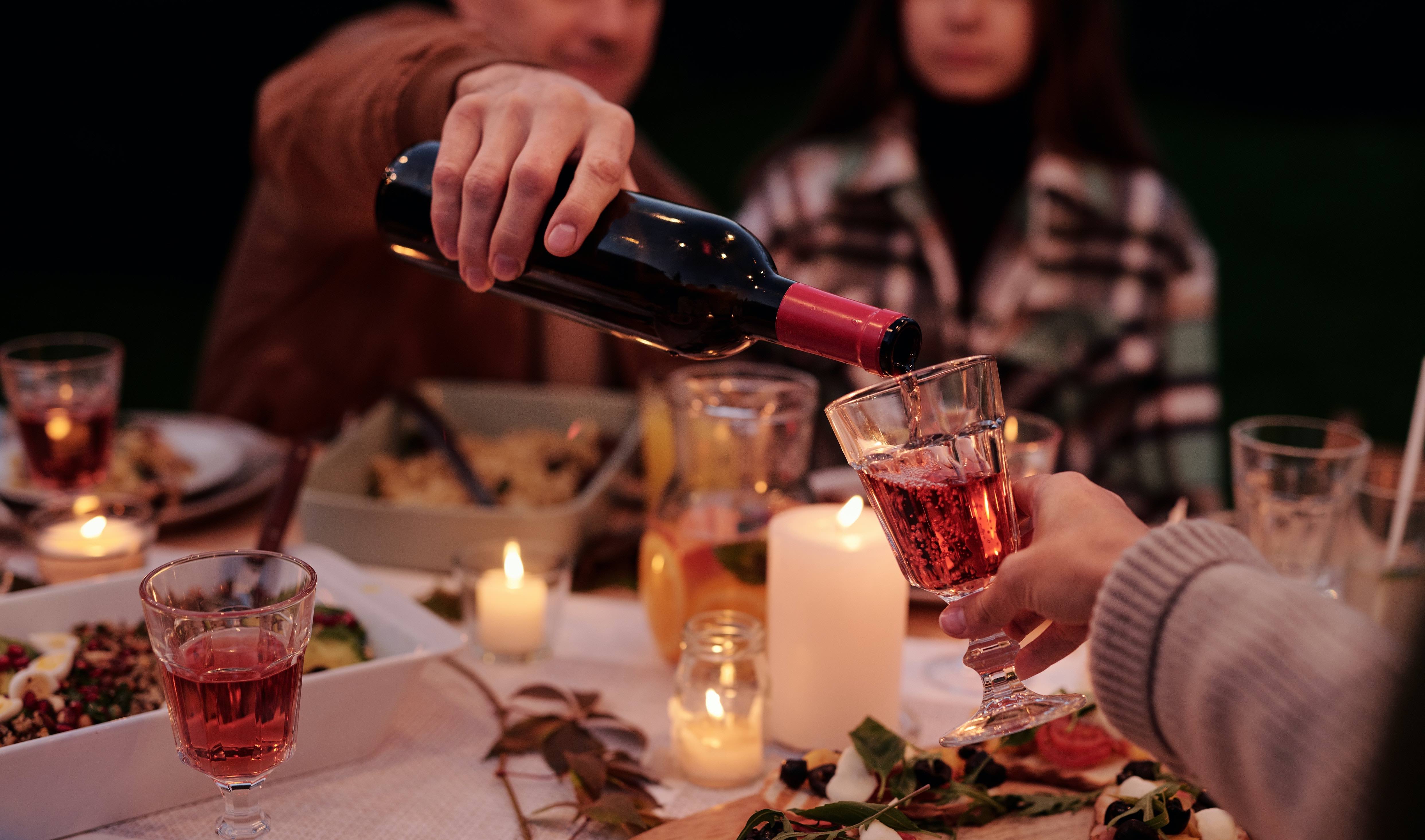 Wine is poured into a glass over a full dinner table