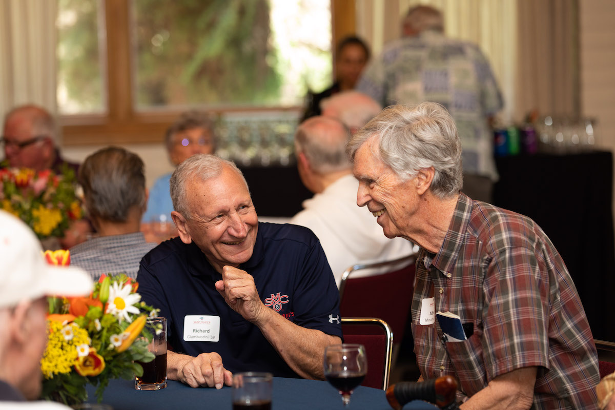 Two alumni share a laugh sitting around a table