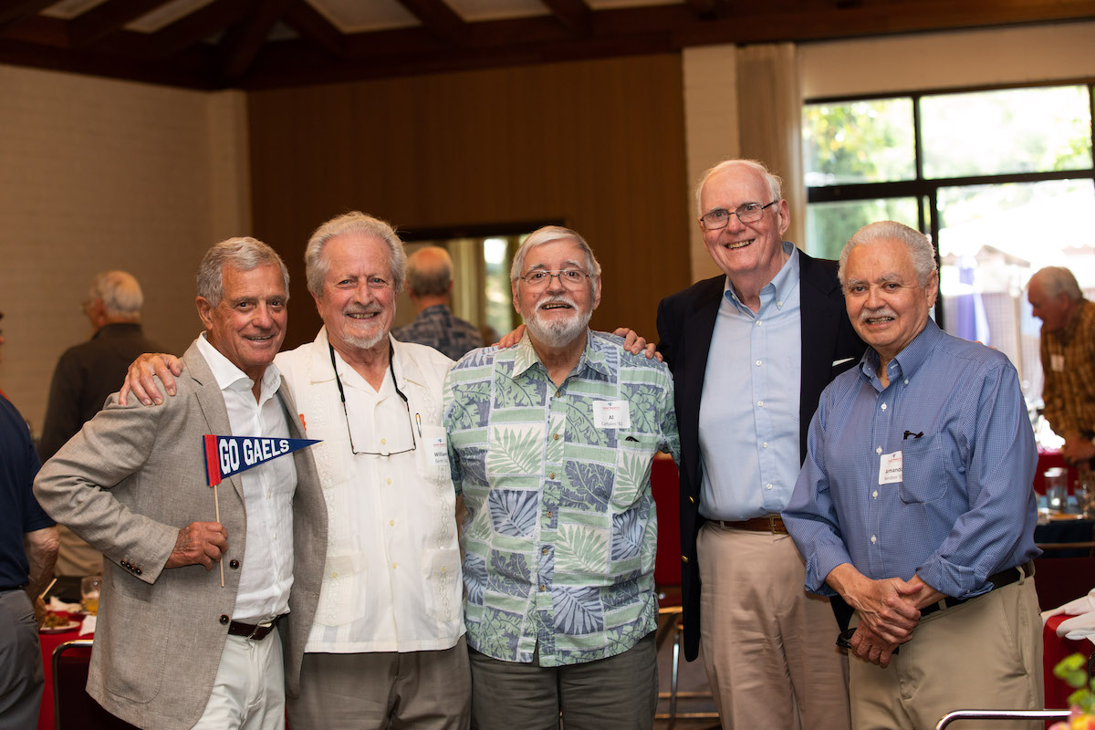 Five alumni smile at the camera, one holding a Go Gaels pennant