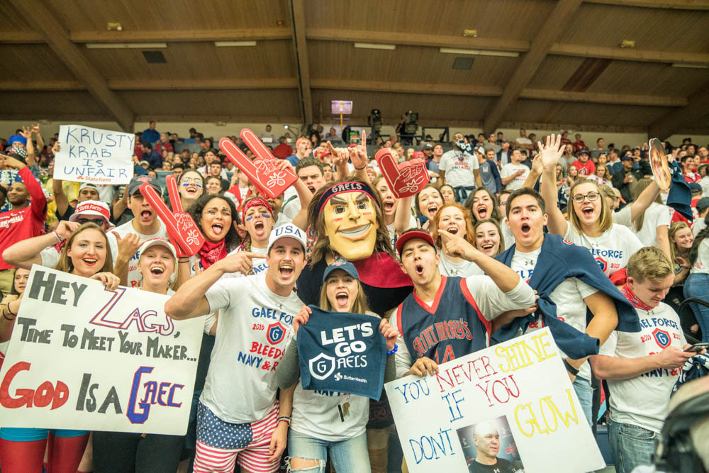 Students cheering and holding signs at a basketball game with Gideon the mascot