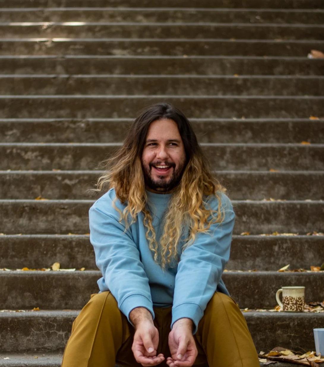 Andrew Merrell sitting at the bottom of stairs, smiling and looking to the right