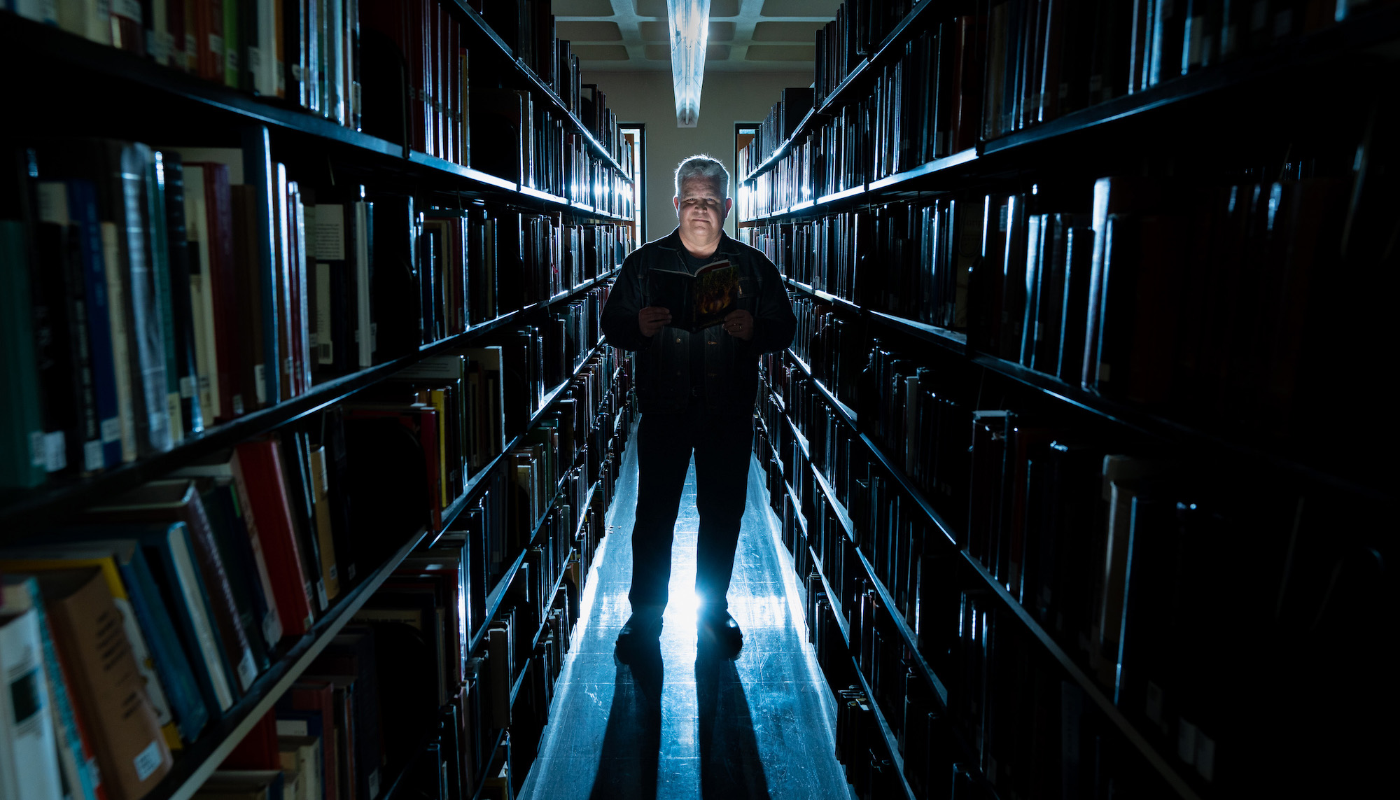 Norm Partidge in library stacks with dramatic lighting, October 2023