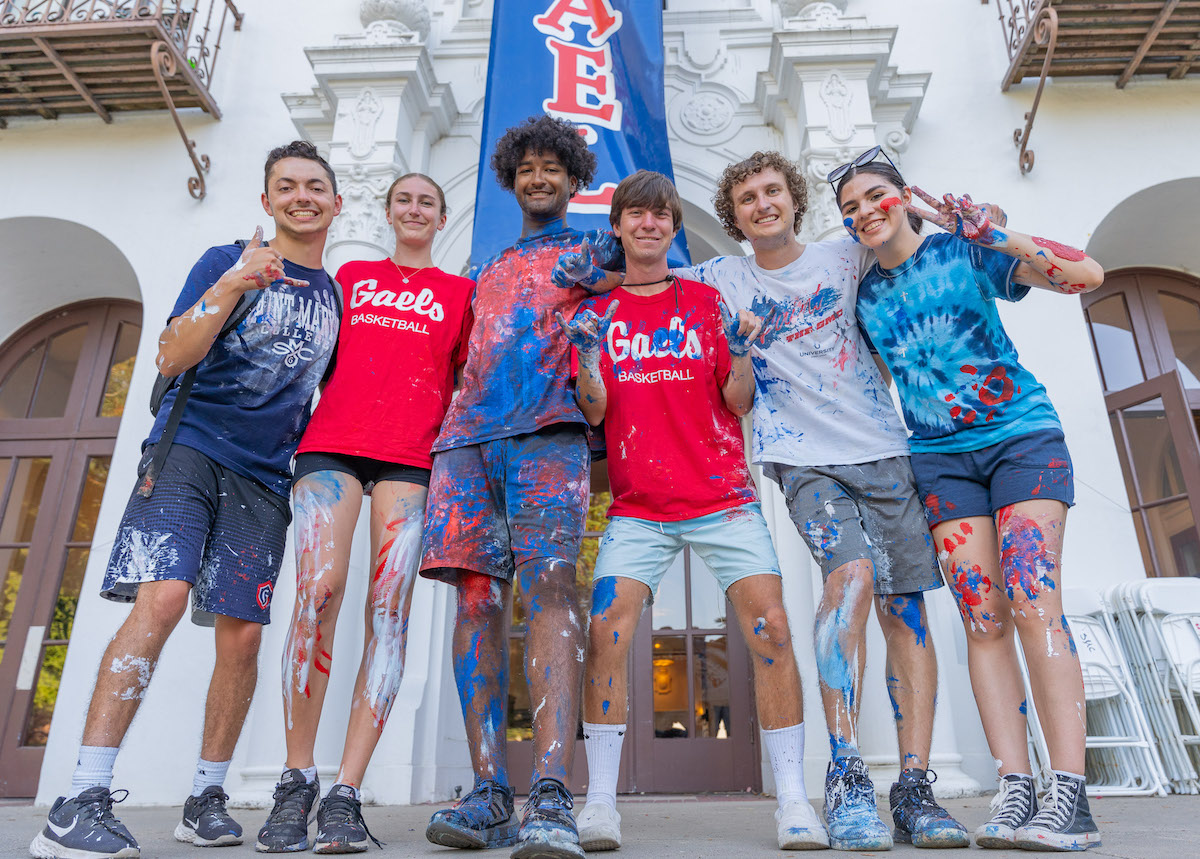 Six students covered in paint in front of the sign GOD IS A GAEL