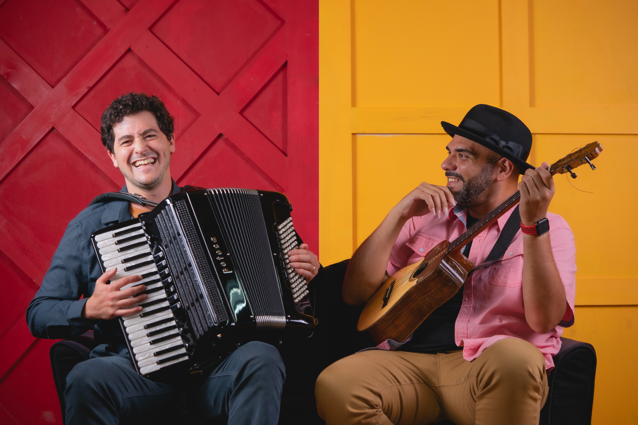 Sam Reider and Jorge Glem, laughing in front of a colorful wall