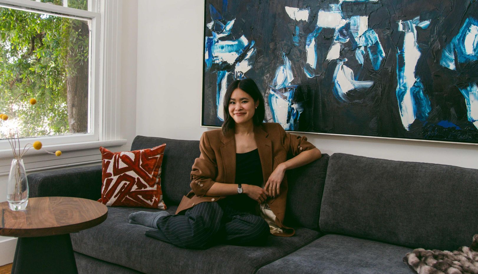 Sierra Nguyen sits on a sofa with a large, blue painting behind her