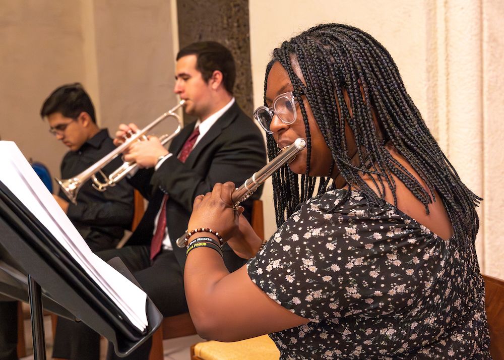 A student playing a flute and a student playing the trumpet dressed in dressy black clothes.