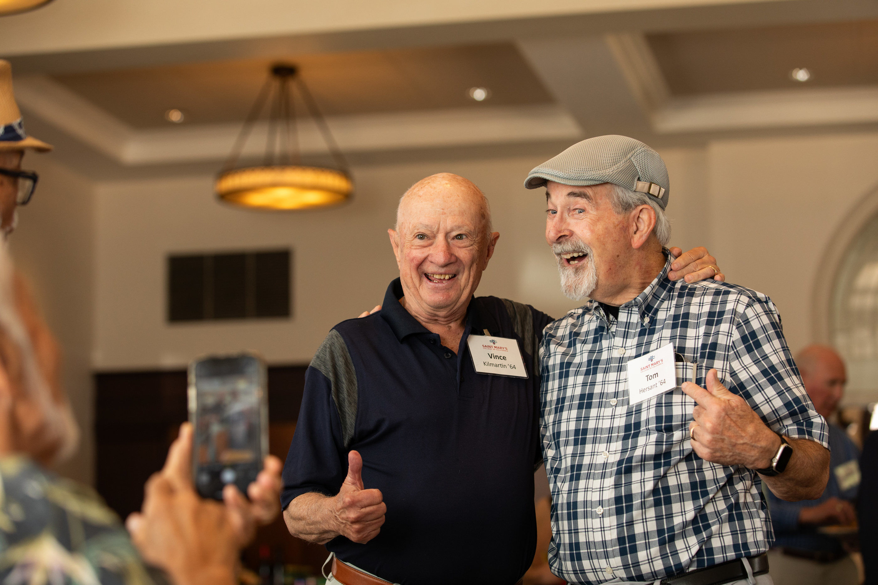 Two older male alumni smile theatrically for a photo