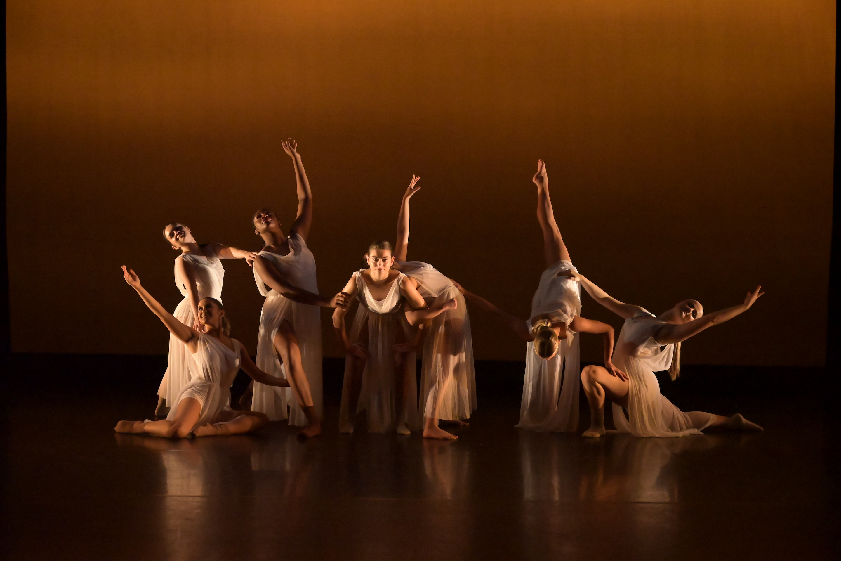 dancers in white flowy dresses with a yellow glow in the background