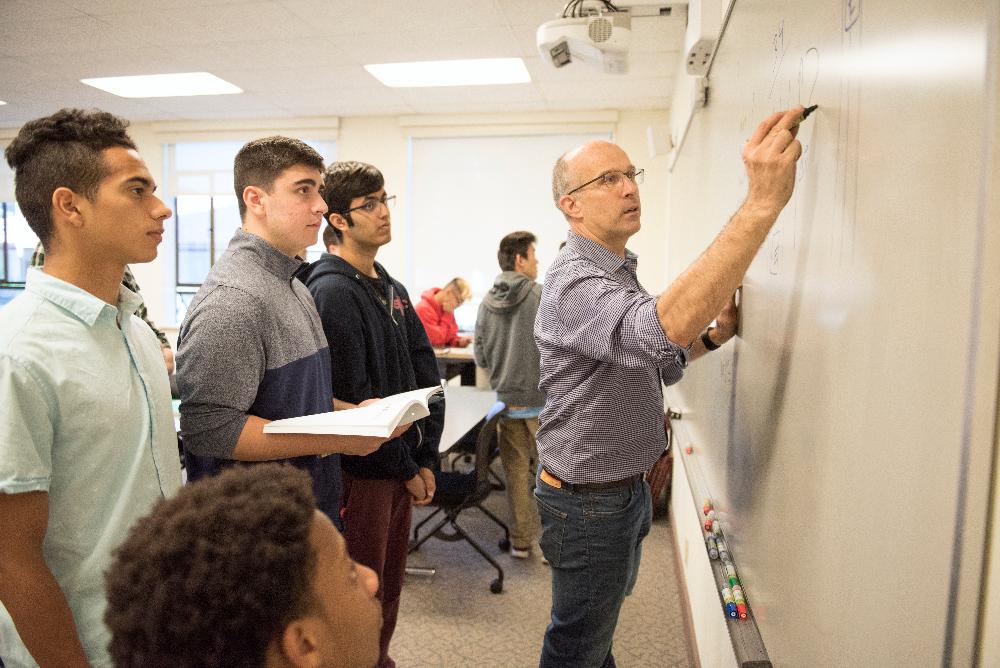 Students looking on as professor writes on whiteboard