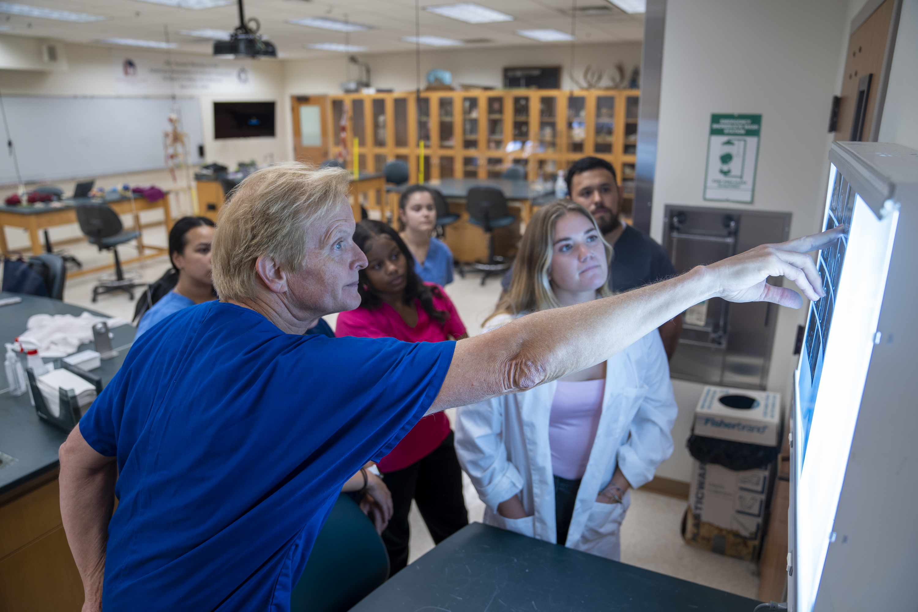 Professor in blue scrubs pointing to an Xray as students look at it in the foreground