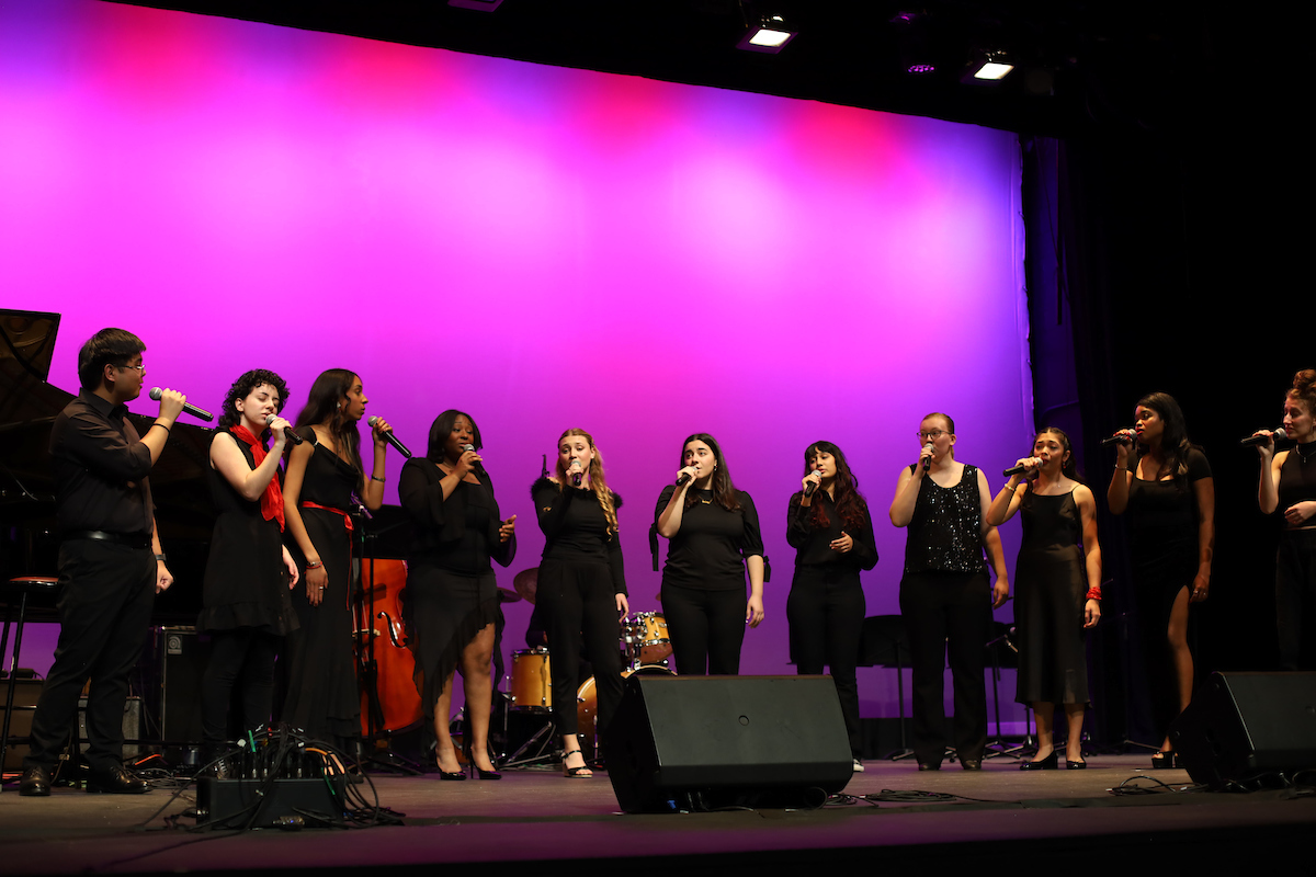 Jazz singers dressed in black with red accessories sing on LeFevre Stage with a purple hue on the cyc behind them.