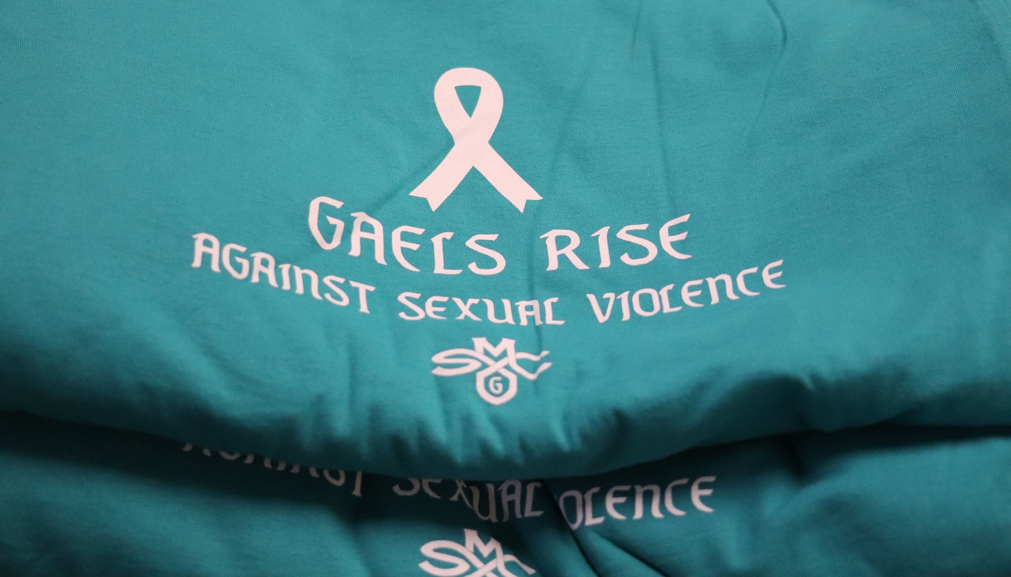 Teal T-shirts with a white ribbon and the words "Gaels Rise Against Sexual Violence"