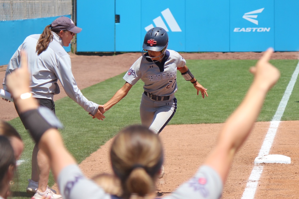 Softball payer Mia Zabat rounds third and coach Sonja Garrett congratulates her in May 2025