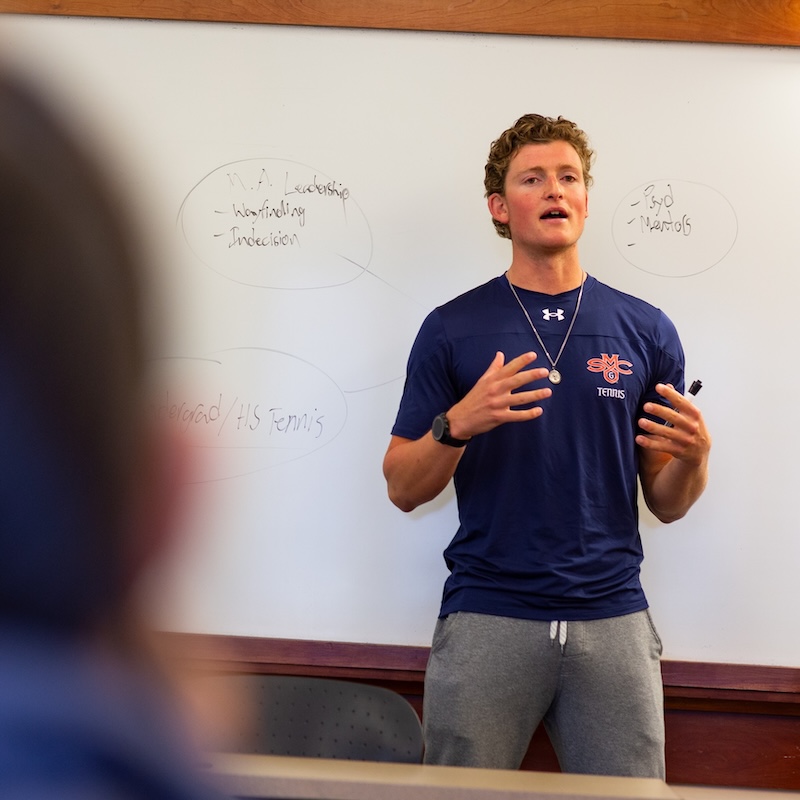 SMC Men's Tennis player in front of white board in class on leadership