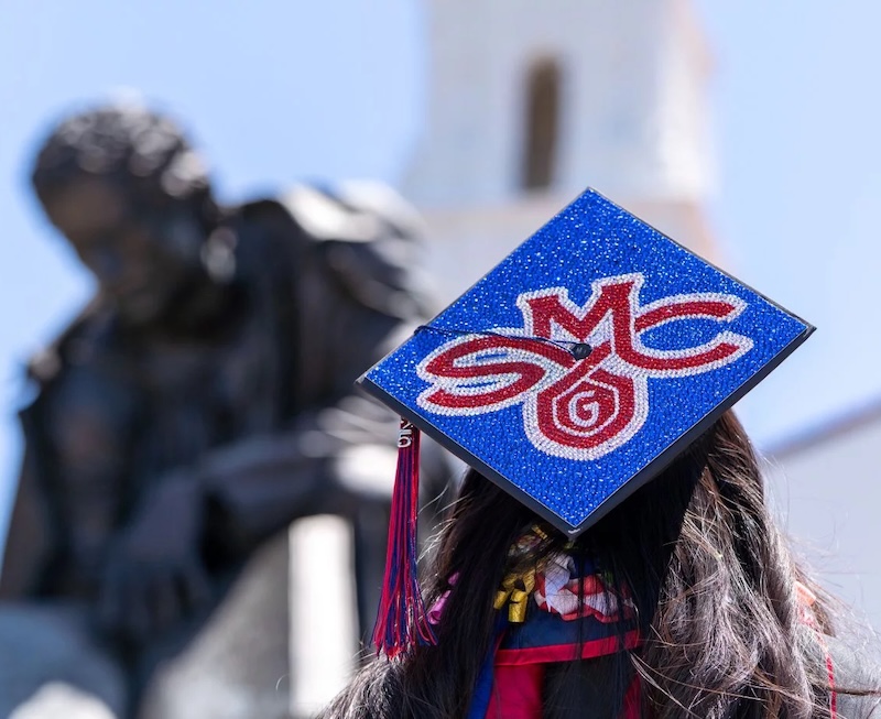 Student wearing mortarboard with SMC logo in front of chapel, May 2025