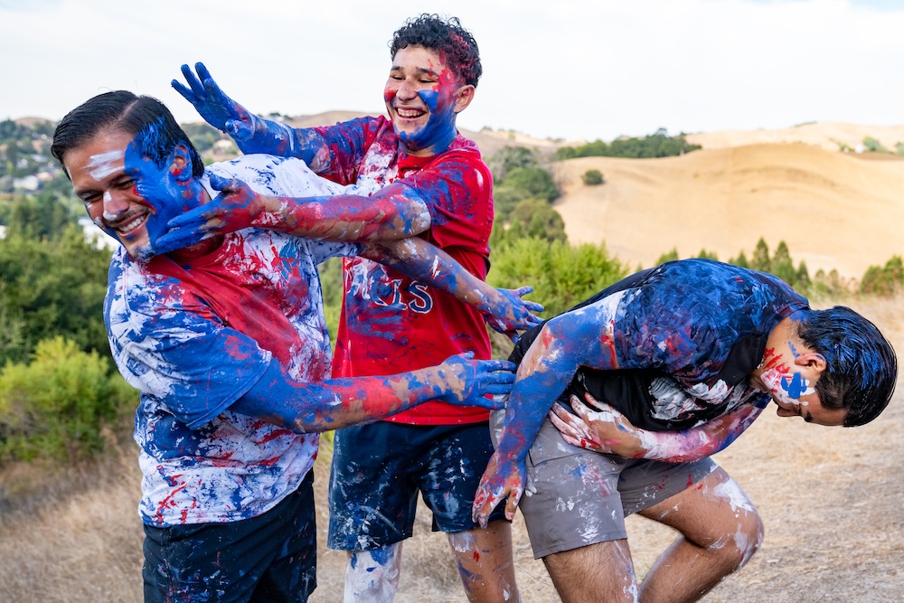 Three male students covered in paint as part of Paint the SMC in 2025