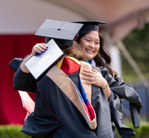 Student Samantha Mae Flores hugs another graduate at 2025 commencement