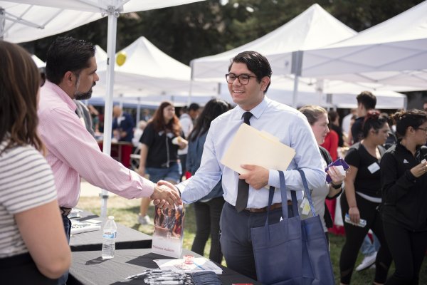 A student in a tie smiling and shaking hands with a man