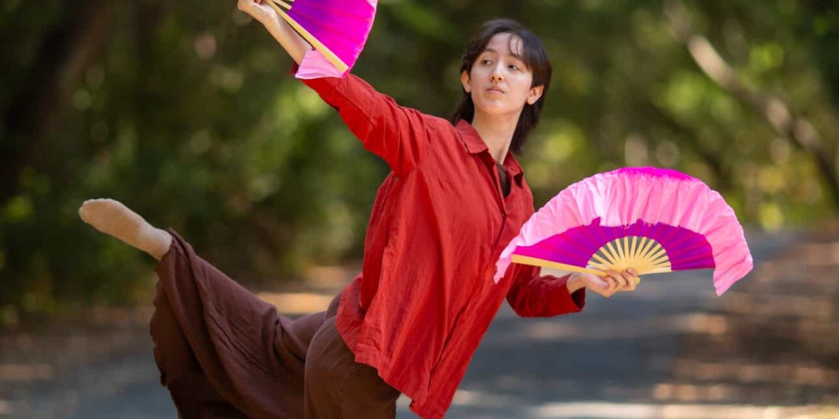 Anya tang poses outdoors with trees in the background and Japanese fans in his hands