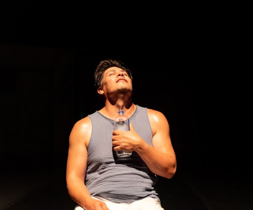Rogelio Lopez dance faculty in performance of breath. Kneeling clutching glass bottle.