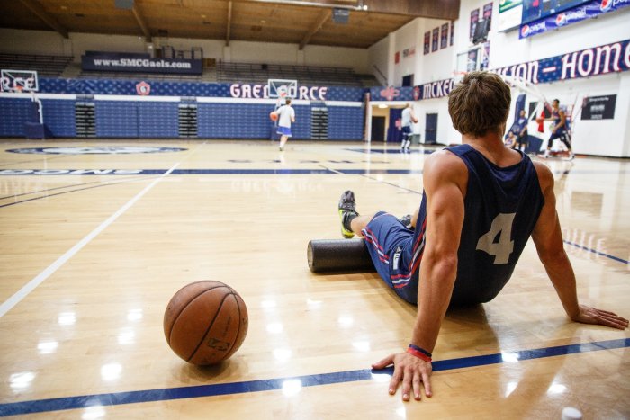 An SMC basketball player leaning back on the court with a basketball sitting to his left.