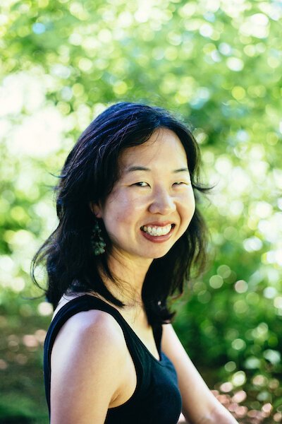 Headshot of Visiting Writer Shelley Wong smiling in front of a lush background of greenery.