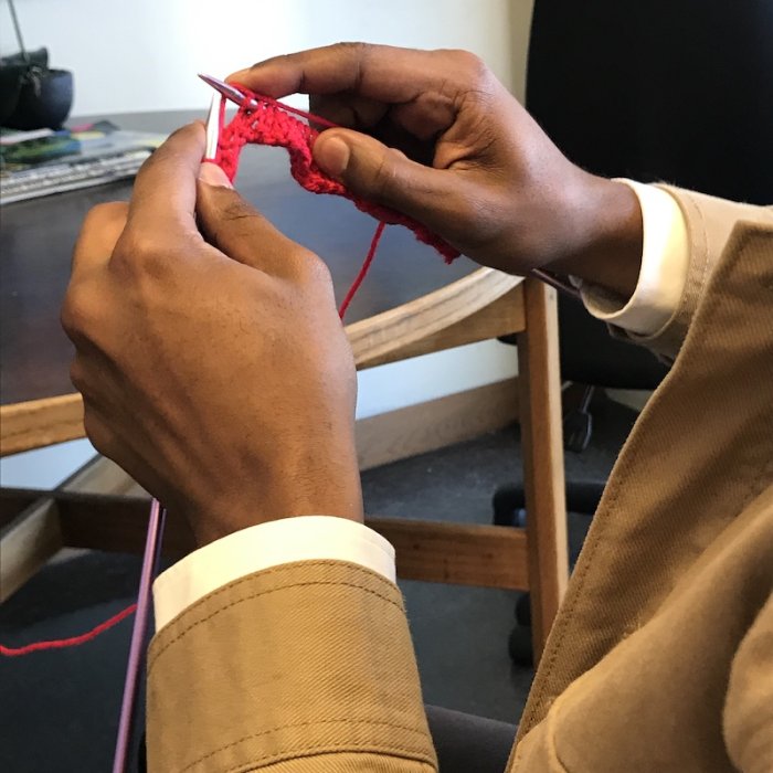 hands of a student knitting a red scarf