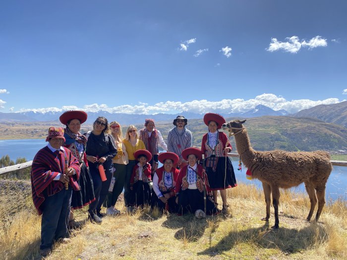 A group of students and adults stand next to an alpaca in Peru
