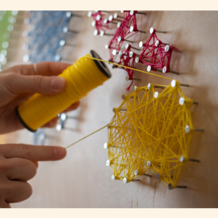 hands creating designs using string and nails