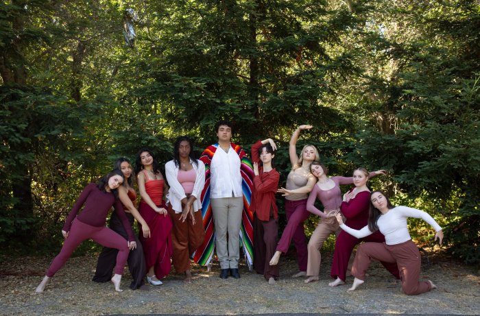 The SMC senior dancers hold poses outside in front of a forest of trees.